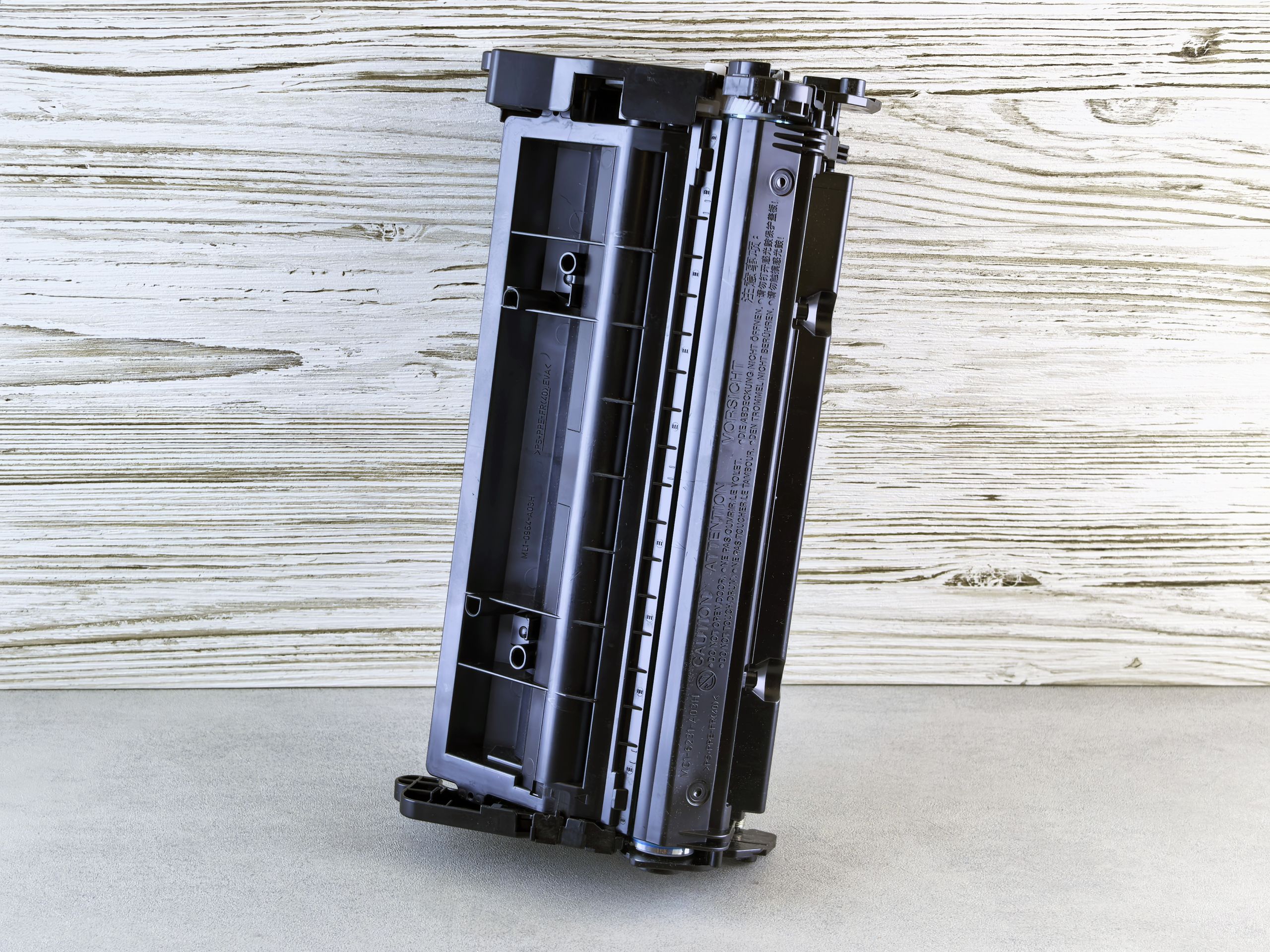 Close-up of a black printer toner cartridge against a rustic wooden background, side view.