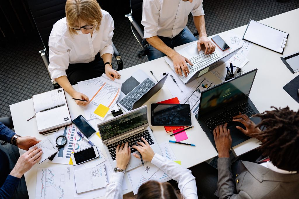 Vibrant office teamwork scene with laptops, documents, and diverse professionals in a meeting.